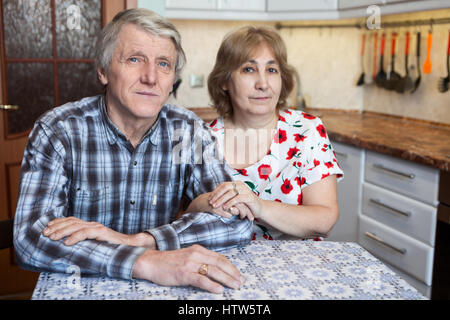 Caucasian couple âgé assis à la table de cuisine et looking at camera Banque D'Images