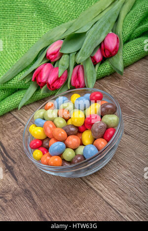 Bonbons colorés dans un bol en verre avec tulipes rouges sur un fond de bois Banque D'Images