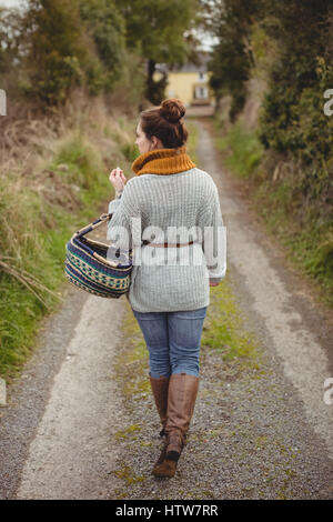 Femme avec panier de marcher sur la route entre les champs Banque D'Images