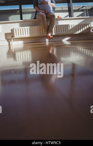 Femme enceinte assis près de fenêtre dans salle de séjour Banque D'Images