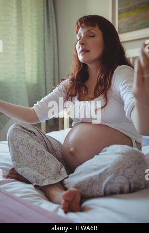Pregnant woman performing yoga on bed Banque D'Images