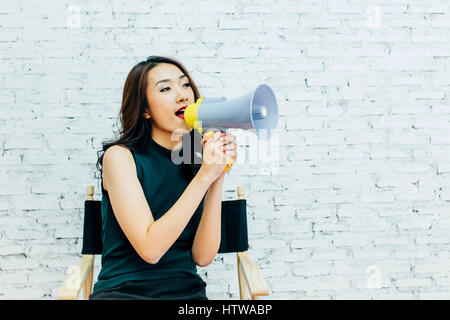 Asian business woman shouting avec mégaphone sur fond de mur de briques blanches Banque D'Images