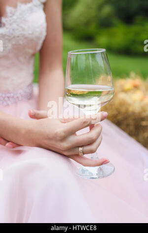 Femme main tenant le verre à vin blanc. Mariée est assis sur sur une balle de foin. Banque D'Images