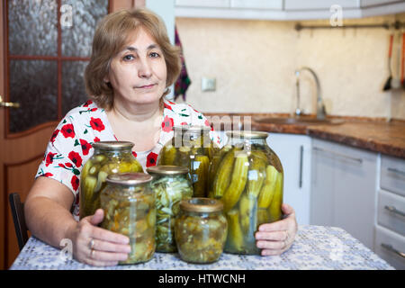 Portrait of middle-aged woman russe est assis à une table de cuisine avec des pots de verre pleine de cornichons Banque D'Images