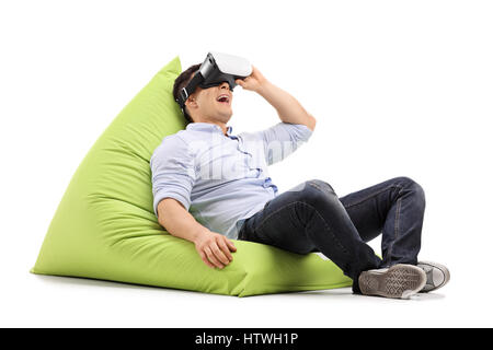 Joyful guy using a virtual reality headset and lying on a beanbag isolated on white background Banque D'Images