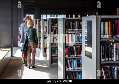 Couple de personnes âgées à la livre à lire à partir de rangées de livres dans les étagères de la bibliothèque publique à Banque D'Images