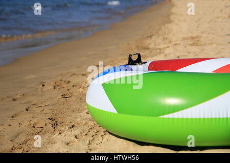 Anneau gonflable coloré sur une belle plage de sable dans le soleil d'été, vert, rouge, blanc, bleu. Banque D'Images