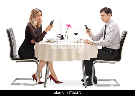 Jeune homme et femme assis à une table de restaurant et en regardant leurs téléphones isolé sur fond blanc Banque D'Images