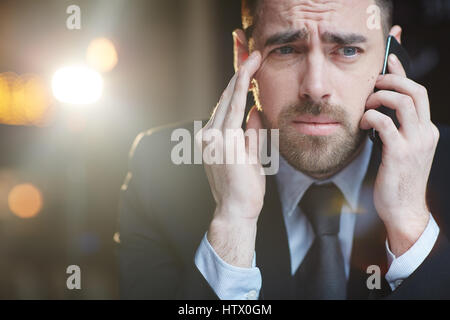 Portrait of businessman wearing barbu moderne costume formel à la confusion et a souligné lors de la communication par téléphone mobile avec problème client contre bla Banque D'Images