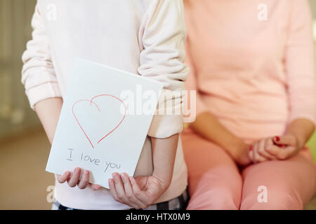 Little girl holding self-made Greeting card for mother day behind back Banque D'Images