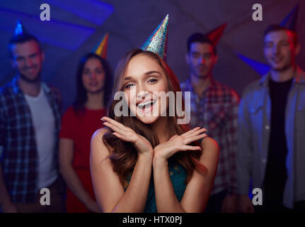 Cheerful girl dans anniversaire cap sur fond de ses amis Banque D'Images