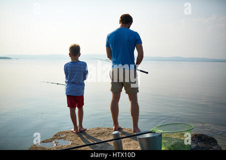 Retour Voir portrait de l'homme bien bâti musculaire réglage de la canne à pêche en se tenant sur le lac avec son petit-fils, le partage hobby sur journée ensoleillée Banque D'Images