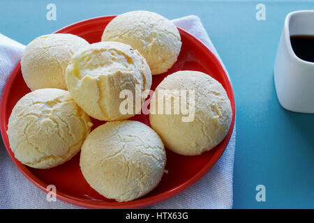 Gros plan sur la bouche-arrosage pain fromage brésilien (Pao de Queijo") sur la plaque rouge, servi avec une tasse de café expresso dans une coupe carré, sur bleu backgroun Banque D'Images