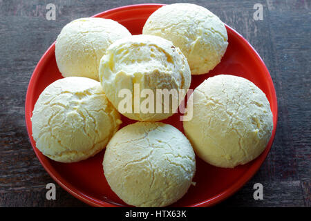 Gros plan sur la bouche-arrosage pain fromage brésilien (Pao de Queijo") sur la plaque rouge, sur une table en bois grunge Banque D'Images