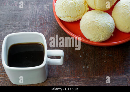 Gros plan sur la bouche-arrosage pain fromage brésilien (Pao de Queijo") sur la plaque rouge, sur une table en bois grunge, servi avec une tasse de café espresso carré Banque D'Images