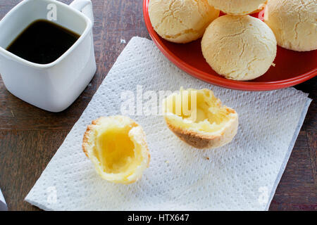 Gros plan sur la bouche-arrosage pain fromage brésilien (Pao de Queijo) réduit de moitié, sur du papier blanc, serviettes autres pains sur la plaque rouge, sur une table en bois, grunge Banque D'Images