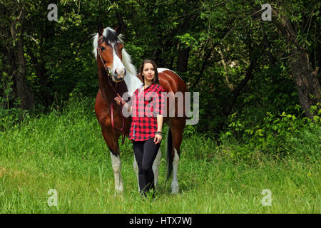 Happy country girl prendre soin de son cheval sur la ferme forestière Banque D'Images