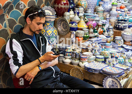 Fes, Maroc. Vendeur céramique contrôler son téléphone cellulaire, boutiques dans le souk du henné, Fes El-Bali. Banque D'Images