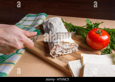 Woman's hand avec couteau dans ce mince coupe pain pita arménienne ou enveloppé lavash tomate, fromage cottage ou fromage, viande de poulet, tomates et fines herbes - Banque D'Images