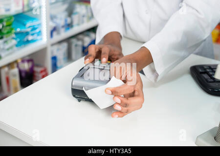 Pharmacien holding réception tout en appuyant sur le bouton du lecteur de carte Banque D'Images