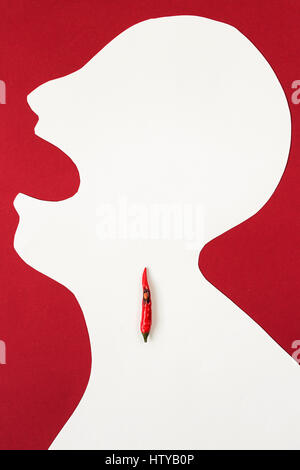 Le contour de la personne coupé d'Livre blanc sur un fond rouge avec une bouche ouverte et piment rouge se trouvant à l'intérieur de lui. concept froid, mal de gorge, brûlant dans une gorge, haut Vue, télévision lay. Banque D'Images