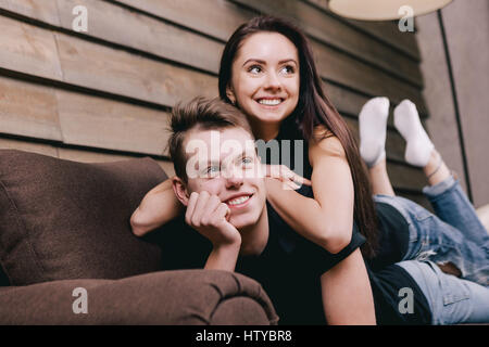 L'homme est allongé sur le ventre sur la table marron, pour soutenir la tête dans ses mains. jolie fille se trouve sur son petit ami. Banque D'Images