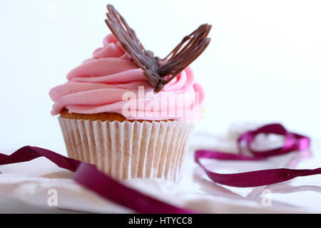 Un fait biologique, frais, vanille Glace fraise cupcake dans de doux tons de rose avec une touche de violet et d'un délicieux glaçage décoration sur le chocolatebutterfly Banque D'Images