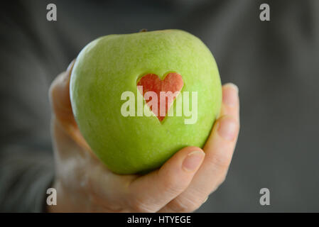 Woman's hand holding a Green Apple avec coeur rouge Banque D'Images