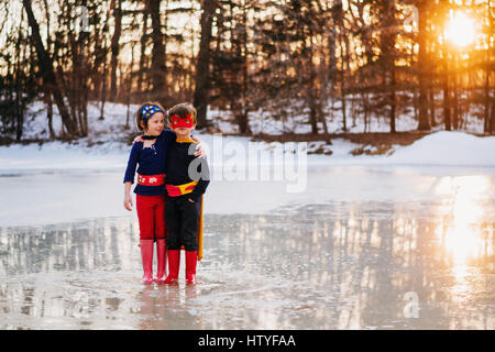 Garçon et fille debout sur lac gelé wearing superhero costumes Banque D'Images