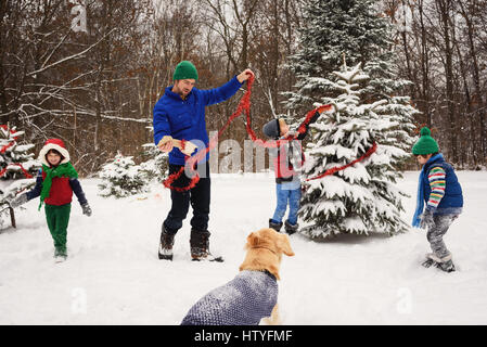 Père et trois enfants décorer un arbre de Noël dans le jardin avec golden retriever dog watching Banque D'Images