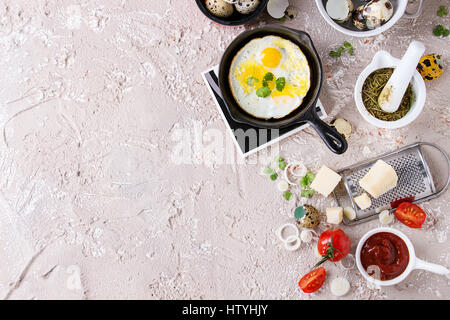 Petit-déjeuner avec des oeufs de cailles dans carter en fonte de fer, tomates cerises, oignons, sauce ketchup, les assaisonnements dans le mortier, râpe à fromage, la coquille en pot. Beige Banque D'Images