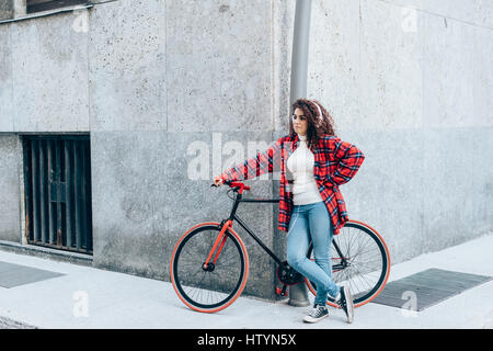 Jeune belle mixed race woman listening music avec des écouteurs s'appuyant sur son vélo - sportive, concept musique Banque D'Images