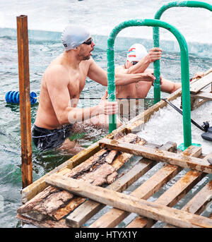 SAHYURTA, région d'Irkoutsk, RUSSIE - Mars 11,2017 : Tasse de Baikal. Les compétitions de natation d'hiver. Un homme qui sort de l'eau sur les mains courantes sur la glace Banque D'Images