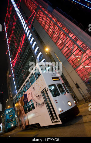 Une vue abstraite d'un tramway de Hong Kong voyageant le long d'une rue dans le quartier des affaires avec des gratte-ciel en arrière-plan dans la nuit. Banque D'Images