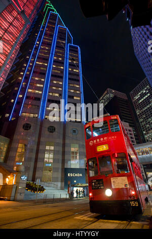 Une vue abstraite d'un tramway de Hong Kong voyageant le long d'une rue dans le quartier des affaires avec des gratte-ciel en arrière-plan dans la nuit. Banque D'Images