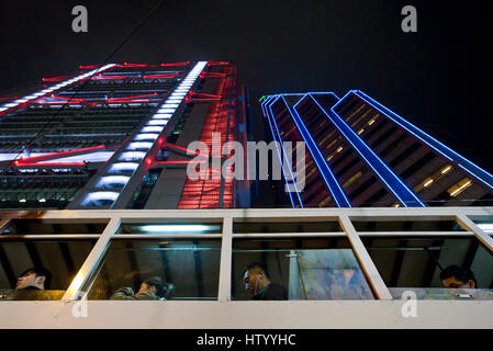 Une vue abstraite d'un tramway de Hong Kong avec 4 passagers navetteurs voyageant le long d'une rue avec des gratte-ciel en arrière-plan dans la nuit. Banque D'Images