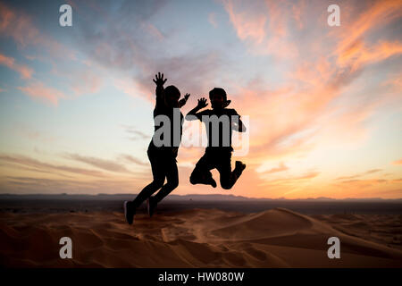 Silhouette d'un couple de saut au coucher du soleil sur les dunes du désert du Sahara à Merzouga - Maroc Banque D'Images