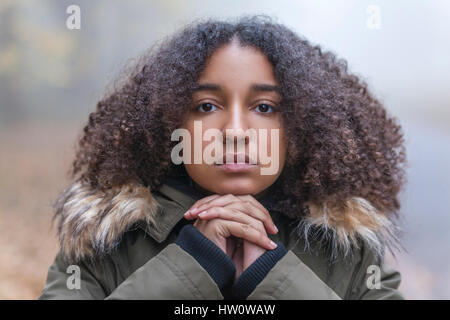 Portrait plein air de belle mixed race African American girl adolescent enfant féminin reposant sur ses mains à l'extérieur dans un parc à jour brumeux Banque D'Images