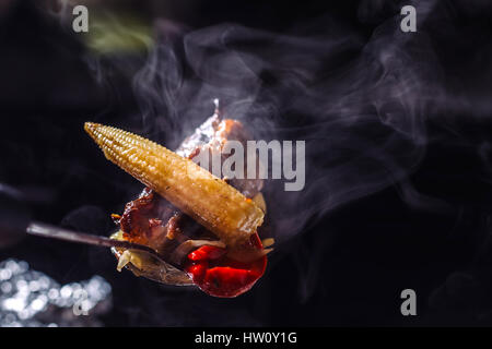 Smokeyshaesya la viande sur une cuillère, avec des épis de maïs et le poivre. Fond noir. Banque D'Images