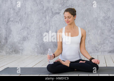 Sensation de soif. Fatigué des jeunes femmes en tenue de sport de l'eau potable et assis sur le tapis d'exercice Banque D'Images