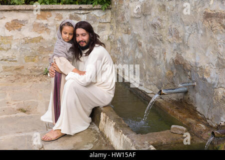 Scène biblique quand Jésus dit, laissez venir à moi les petits enfants, la bénédiction d'une petite fille. Reconstitution historique à un vieux puits. Banque D'Images