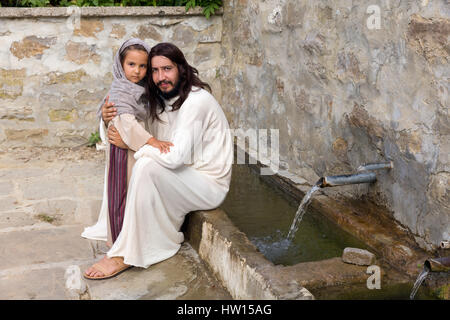 Scène biblique quand Jésus dit, laissez venir à moi les petits enfants, la bénédiction d'une petite fille. Reconstitution historique à un vieux puits. Banque D'Images