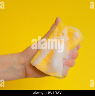 La main avec une éponge avec de la mousse sur fond jaune Banque D'Images