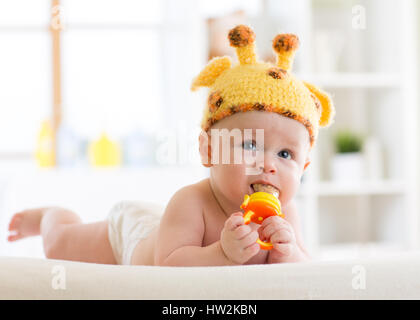 Funny baby boy in girafe hat allongé sur le ventre en pépinière. Petit enfant à l'aide de jouet grignoteur. Banque D'Images