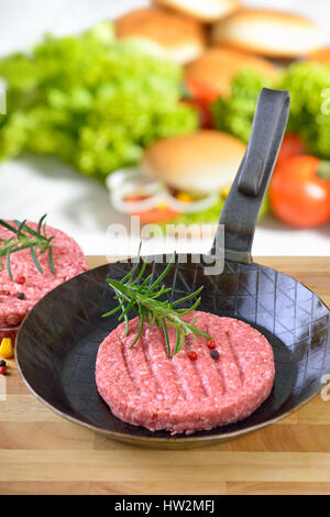 Burger de matières premières dans un patty poêle de fer prêt à fry, certains ingrédients burger dans l'arrière-plan Banque D'Images