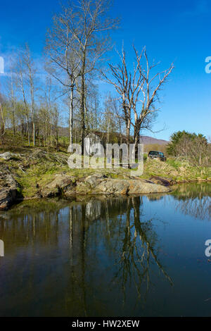 Lac avec vieux camion sur le côté et une ferme abandonnée dans les arbres Banque D'Images