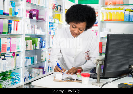 Jeune femme chimiste writing on clipboard at counter in pharmacy Banque D'Images