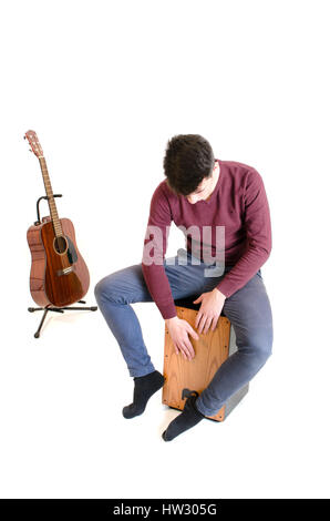 L'homme musicien adolescent assis sur un Cajon et jouer avec une guitare à l'arrière isolé sur fond blanc Banque D'Images