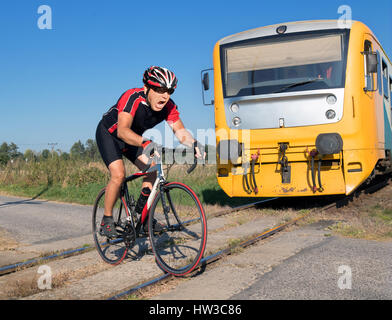 Cycliste est terrifié par le train avant de se précipiter sur les voies. Choqué biker ride un passage à niveau à l'avant d'un train qui approche. Le train régional Banque D'Images