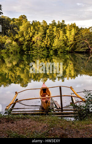 Un pêcheur traditionnel bateau amarré la pompe en place que les couchers de soleil sur une rivière bordée d'arbres comme miroir. Banque D'Images